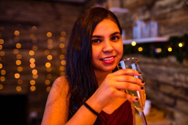 Stüdyoda alkol içen Hintli kadın Ladin Noel ağacı ışıkları arka planında çelenk vurdu.