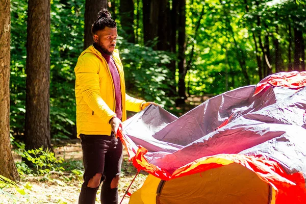 Africano americano en amarillo jacker poner en un tienda en bosque — Foto de Stock