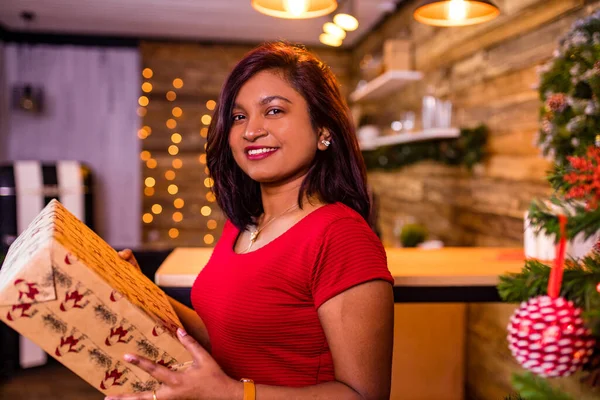 Indianerin in rotem Kleid hält große Schachtel mit Schale im Wohnzimmer Fichte Weihnachtsbaum Lichtergirlanden Hintergrund — Stockfoto