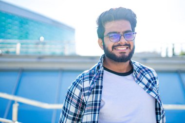 Yazın şehir merkezinde şık, kareli tişörtlü ve beyaz tişörtlü Arap genç bir adam.