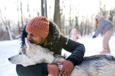 Karışık ırk adamı kış parkında köpeğine sarılıyor.