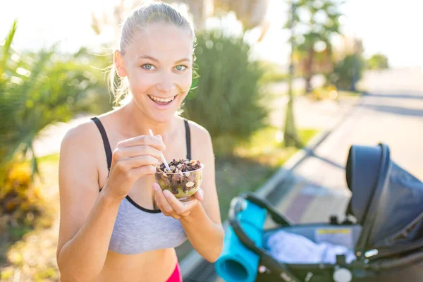 blonde woman holding yoga mat and vegan yogurt ice cream with cocoa bean chocolate and peanuts in tropics background