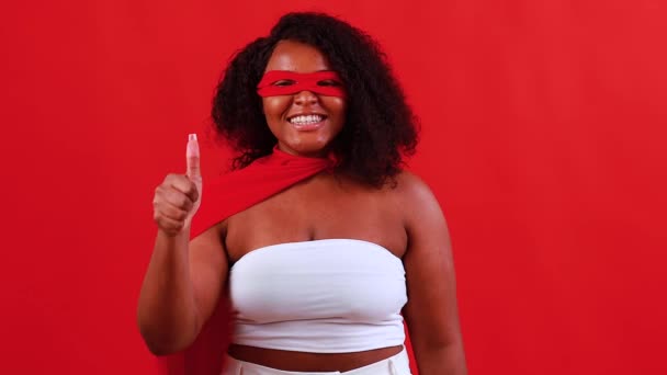 Latin hispanik wanita dalam masker mata merah dan jubah superhero panjang di latar belakang studio — Stok Video