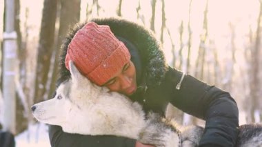 Karışık ırk adamı kış parkında köpeğine sarılıyor.