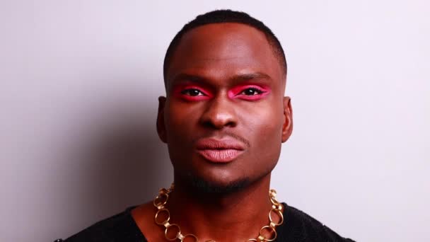 Afro amerikaanse man in jurk stijl met roze oogschaduw en lippenstift crossdressing in fashion show studio achtergrond — Stockvideo