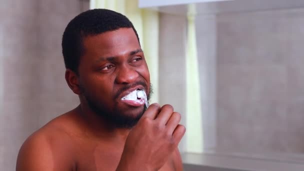 África homem escova de dentes no banheiro olhando para o espelho — Vídeo de Stock