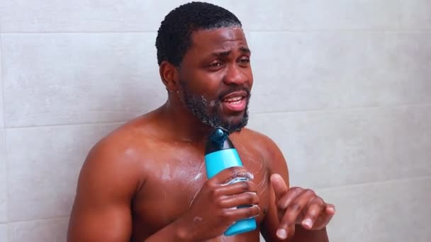Atrakcyjny młody wesoły mężczyzna śpiewa podczas mycia pod prysznicem, trzymając butelkę szamponu — Wideo stockowe