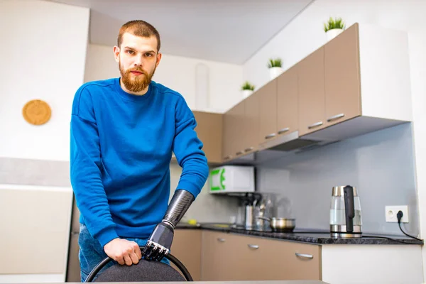 Giovane uomo con le mani cyborg muovendo la sedia e seduto in cucina a casa — Foto Stock