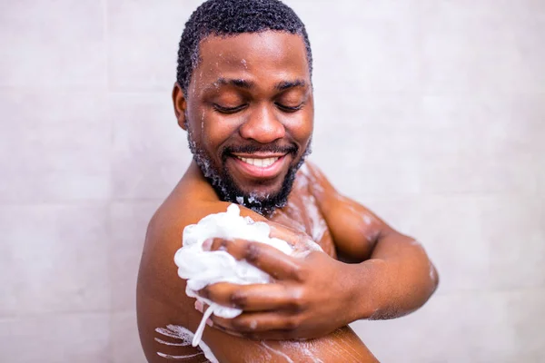 Hombre brasileño lavando cuerpo con esponja de ducha en baño blanco —  Fotos de Stock