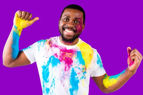 Afro american man celebrate holi festival in violet studio background — ストック写真