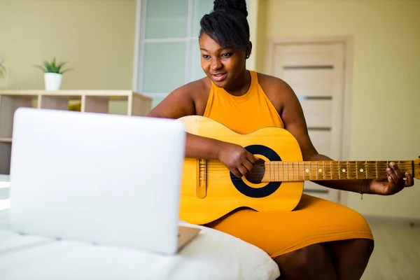 Afrikanska amerikanska kvinna spelar på gitarr wgile sitter i sovrummet — Stockfoto