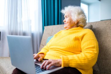 Yaşlı gri saçlı kadın oturma odasında otururken gözlerini kaçırıyor.