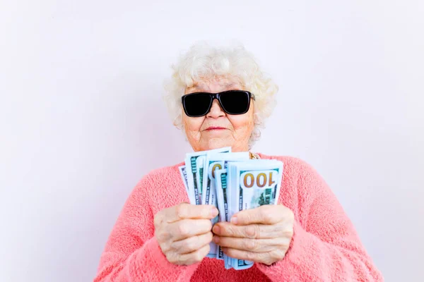 Loira velha senhora desgaste pinl suéter e óculos de sol mostrando dinheiro isolado fundo branco — Fotografia de Stock
