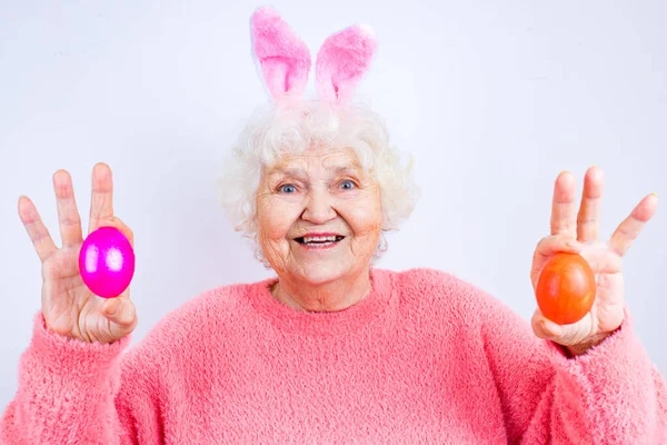 Heureuse femme de 80 ans portant des oreilles de lapin et ayant des œufs de Pâques — Photo