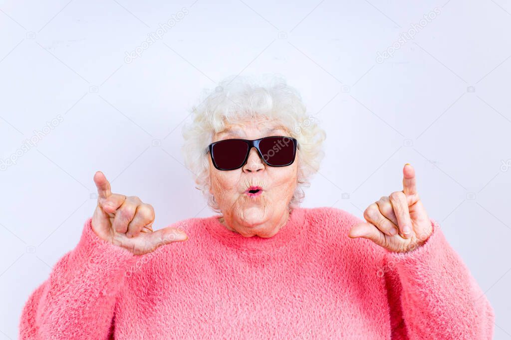 Portrait of funny senior blonde woman in sun glasses and pink sweater on white background
