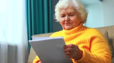 Şok olmuş yaşlı kadın beyaz saçlı oturma odasındaki kanepede oturuyor faturalarla