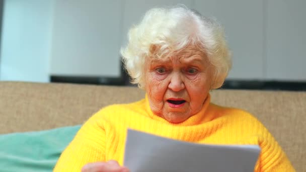 Potrząsnął zdumiony stary kobieta biały siwe włosy siedzi na kanapie w salonie z rachunków — Wideo stockowe