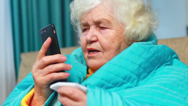 Anciana envuelta en azul en blanco en casa llamando al médico por teléfono — Vídeos de Stock