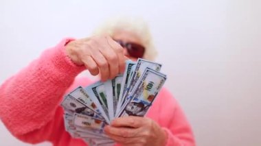 Sarışın yaşlı kadın pembe kazak giyiyor ve güneş gözlüğü takıyor.