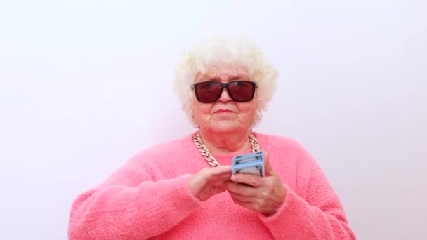 Loira velha senhora usar rosa suéter e óculos de sol jogando dinheiro isolado fundo branco — Vídeo de Stock