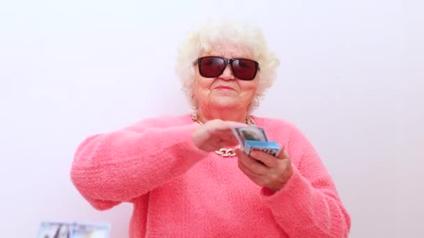 Blonde old lady wear pink sweater and sunglasses tossing money isolated white background — Stock Video