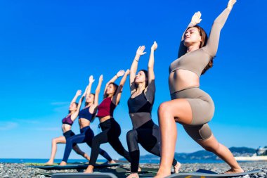 Bir grup genç bayan deniz kenarında yoga yapıyor.