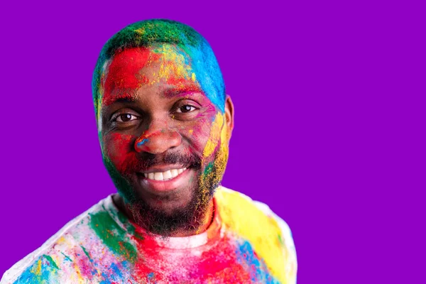 Afro american man celebrate holi festival in violet studio background — ストック写真