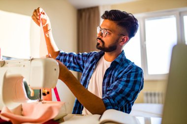 Hintli terzi, yeni apartman dairesinde dikiş makinesiyle eğitim görüyor ve serbest çalışıyor.