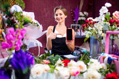 Çiçekçi dükkanında cep telefonu teslimatını kullanan bir kadın çiçekçi.