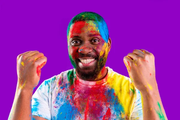 Afro americano homem celebrar holi festival em violeta estúdio fundo — Fotografia de Stock