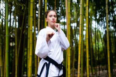 Siyah kuşaklı genç bir kadın dövüş sanatları koçu bambu arka planda.