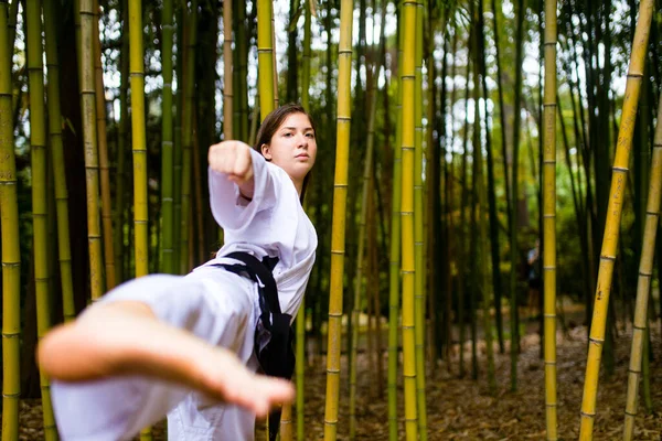 Una mujer joven con un cinturón negro entrenadores en el fondo de bambú de arte marcial al aire libre —  Fotos de Stock