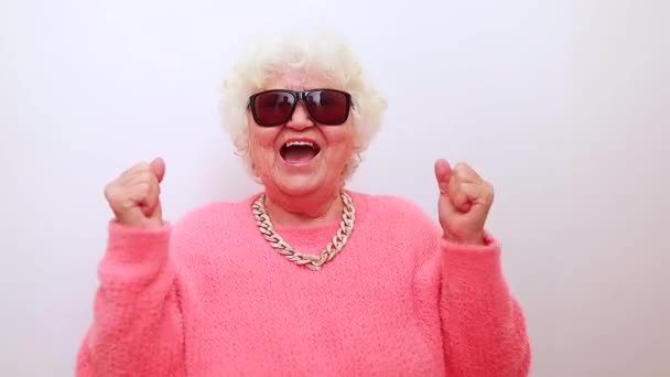 Portrait de drôle surpris femme blonde senior surprise dans des lunettes de soleil et pull rose sur fond blanc s'amuser — Video