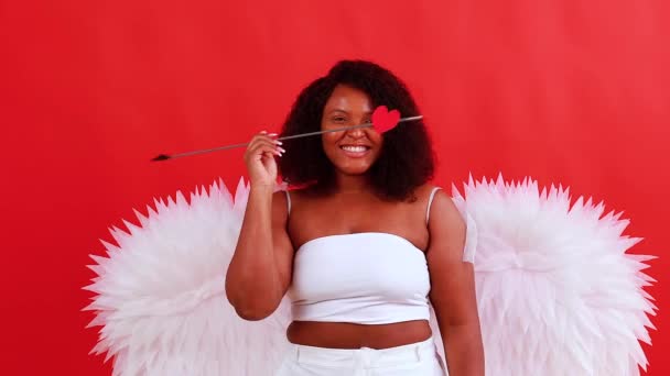 African latin cupid woman in wtite top bra holding bow and arrow in red studio The 14th of February Valentines Day — Stock Video