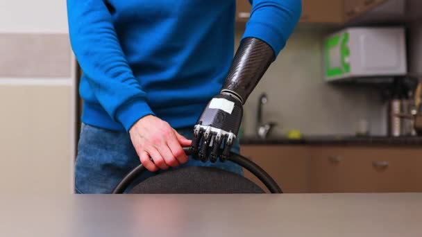 Young man with cyborg hands moving the chair and sitting at kitchen at home — Stock Video