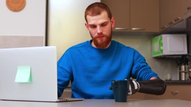 Fiatal szabadúszó üzletember protézissel kéz dolgozik otthon laptop és ivóvíz vagy tea a konyhában — Stock videók