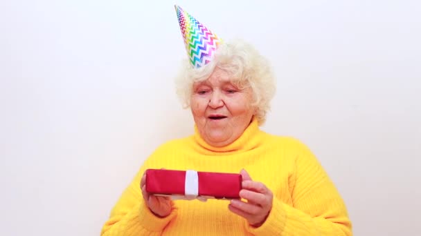 Mulher mais velha com um presente usar camisola amarela e tampão de chifre em um fundo branco — Vídeo de Stock