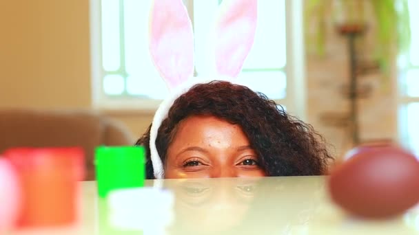 Ung afrikansk amerikansk kvinna bär söta påsk kanin öron i huset gömma sig under bordet — Stockvideo