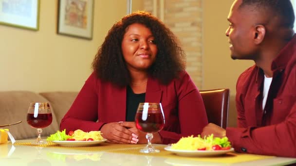 Αφρικάνικο ζευγάρι που τρώει ζυμαρικά ιταλικών τροφίμων στο σαλόνι σε κομψό σακάκι marsala χρώμα και πίνοντας κόκκινο κρασί — Αρχείο Βίντεο
