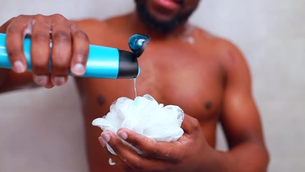 Een jonge Afrikaanse man in de ziel giet shampoo op een spong in slow motion. — Stockvideo