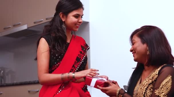 Милая молодая индийская женщина в традиционной этнической одежде дарит подарок сестре в гостиной домашний фон с Новым годом или Дивали — стоковое видео