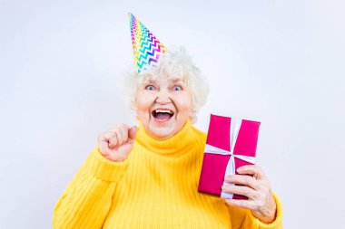 Hediyesi olan yaşlı bir kadın beyaz arka planda sarı kazak ve boynuz şapkası giyer.