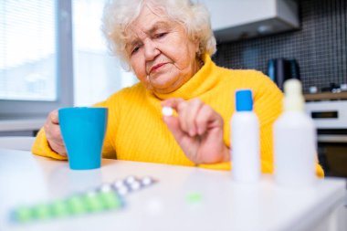 Evindeki ilaç kutusundan hap alan yaşlı bir kadın.
