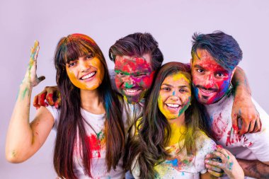 Dört mutlu arkadaş, beyaz arka plandaki stüdyoda geleneksel Holi zamanı geçiriyorlar.