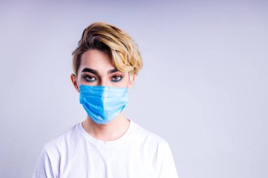 Lüks sarı saçlı, beyaz duvar arkasında muhteşem makyajlı Asyalı bir adamın ikili portresi. Tıbbi yüz maskesi takın.