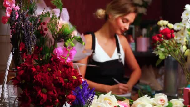 Zierliche blonde Frau in Schürze verkauft Blumen in ihrem eigenen Geschäft — Stockvideo