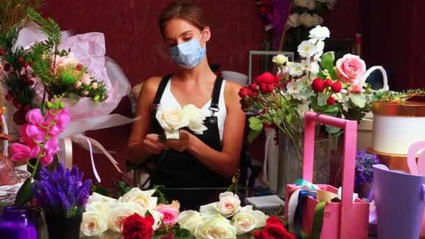 Florist gör bukett för en kund i butiken på våren dag bär medicinsk mask — Stockvideo
