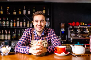 Ekose gömlekli ve önlüklü bir Türk bir barın arkasında duruyor ve çay hazırlıyor.