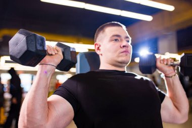 Formda ve kaslı adam spor salonunda dambıllarla antrenman yapıyor.