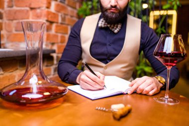 Mutlu erkek şarap üreticisi bir tat alıyor ve kırmızı şarap kalitesini kontrol ediyor.